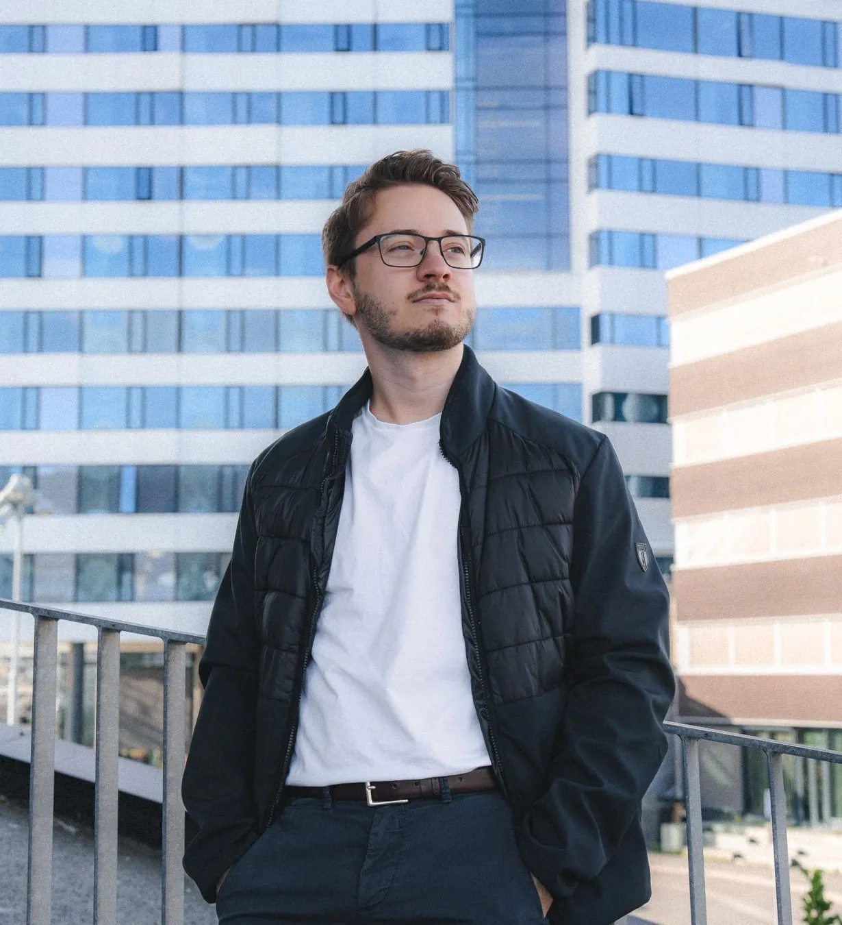 Alexandru on a rooftop, with a white office block with blue windows behind him